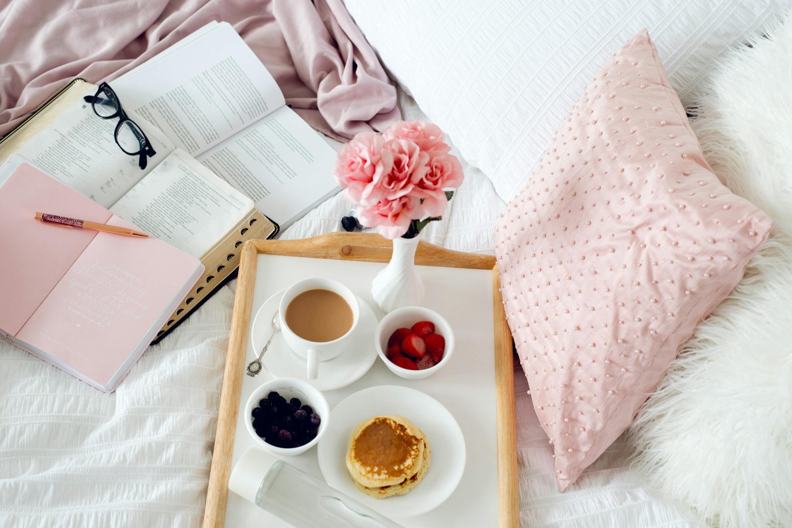 Inviting breakfast in bed setup with coffee, pancakes, and flowers on a cozy tray.