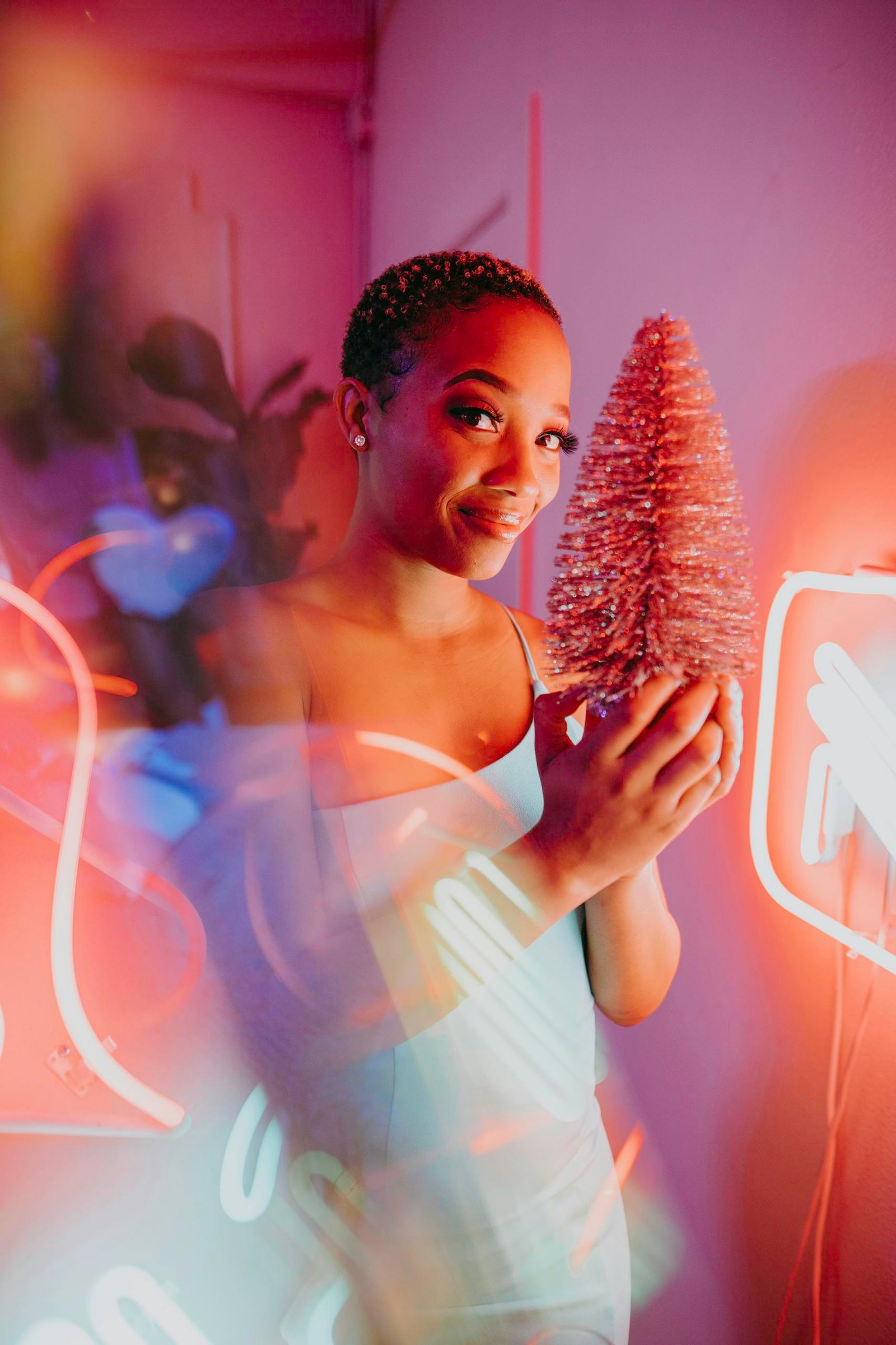 Woman holding a pink Christmas tree with vibrant neon lights.